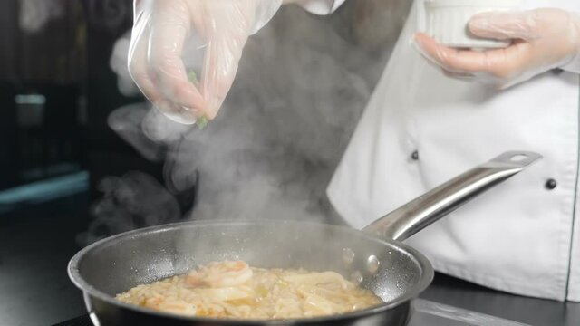 Chef cooking delicious seafood risotto in frying pan. Shot in slow motion. Chef adding fresh herbs into rise on frying pan. Recipe from Traditional Italian cuisine. shrimp risotto in gourmet