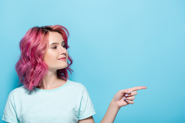 young woman with pink hair pointing aside on blue background