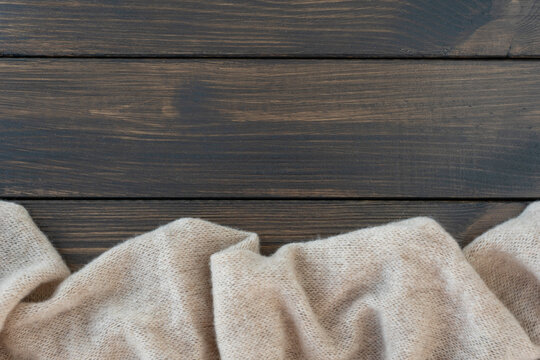 Cosy beige warm wool plaid lie on dark wooden background. Copy space for text or for inscription.  Layot for postcard.