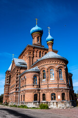 an old red brick church on a hillock near the forest against a blue sky