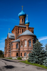 Fototapeta premium an old red brick church on a hillock near the forest against a blue sky
