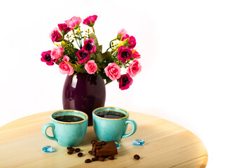 Beautiful flowers in vase with coffee in the morning, two cups of espresso and pieces of milk chocolate  on wooden cutting board  isolated on white background. Side view with copy space for your text.