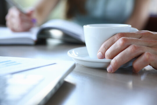 business people in cafe coffee break at table hold cup of coffee in arms closeup