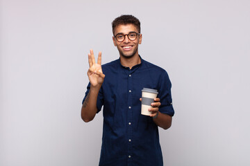 young man with a coffee smiling and looking friendly, showing number three or third with hand...