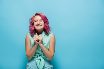 young woman with pink hair smiling on blue background