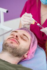 Obraz na płótnie Canvas Cosmetologist is applying white moisturizing mask on man's face using brush in beauty clinic, face closeup. Beauty industry concept. Guy is lying on couch. Beautician woman making spa procedure.