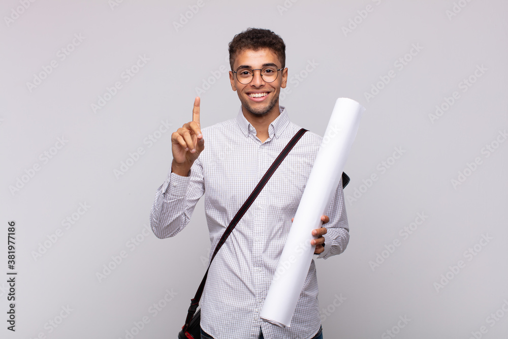 Wall mural young architect man smiling and looking friendly, showing number one or first with hand forward, cou