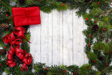 Weihnachtshintergrund, Rahmen aus grünen Tannenzweigen, roten Beeren, Geschenk auf weißem Holz...
