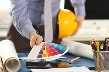 Fototapeta na wymiar Architect Holding Design Color Swatch at Office. Professional Male Building Decorator with Yellow Helmet in Hand. Drawing with Work Engineering Tools and Accessories. Creativity Concept