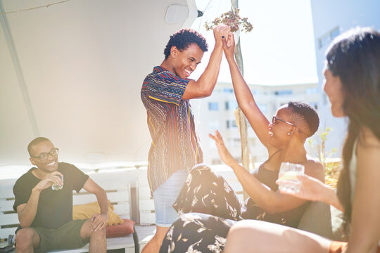 Happy young friends high fiving on sunny rooftop balcony