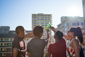 Young friends toasting beer bottles on sunny urban rooftop balcony