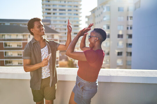 Happy young couple high fiving on sunny urban rooftop balcony - Powered by Adobe