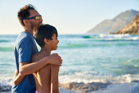 Affectionate father and son hugging on sunny ocean beach