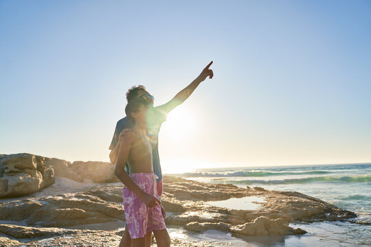Father and son pointing up at sky on sunny ocean beach