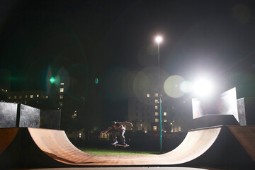Young man skateboarding on ramp at skate park at night