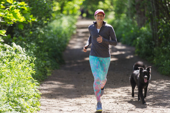 Woman Jogging With Dog On Sunny Trail