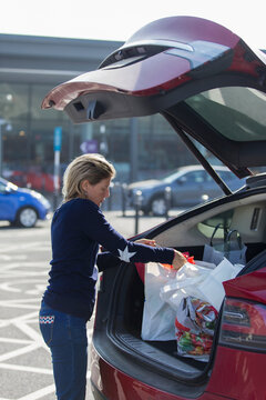 Woman loading groceries into back of car in parking lot