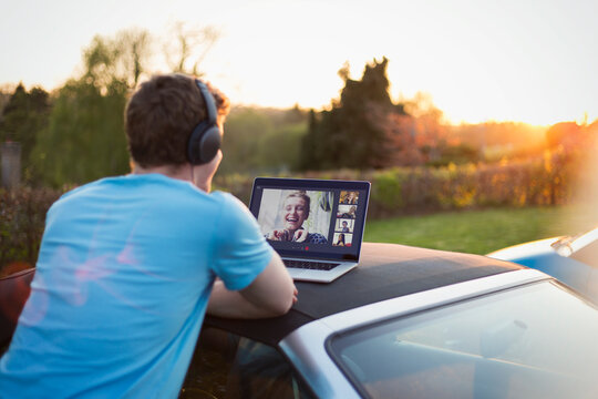Man with headphones and laptop video chatting with friends on car roof