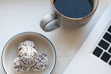 Focus on cup of black coffee and a plate with homemade raw chocolate balls, which is a classic no bake pastry in Sweden and Denmark, next to a laptop keyboard