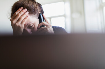 Tired woman talking on telephone at laptop