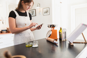 Teenage girl with smart phone baking in kitchen