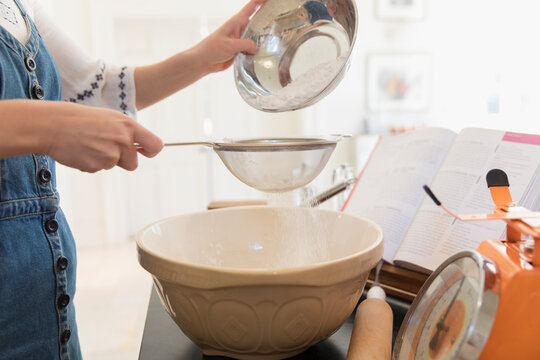 Teenage girl sifting flour for baking in kitchen
