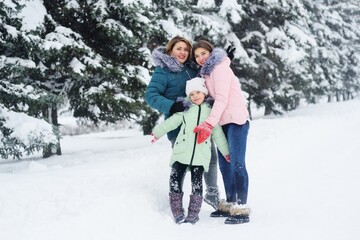 Fototapeta na wymiar family-mother and two daughters have fun and play against the background of snow-covered trees and forests. Winter fun