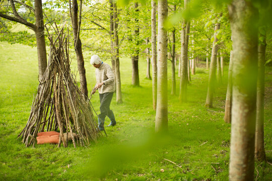 Senior woman making branch teepee in woodland