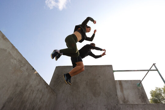 A guy and a girl simultaneously jump from a wall against the sky