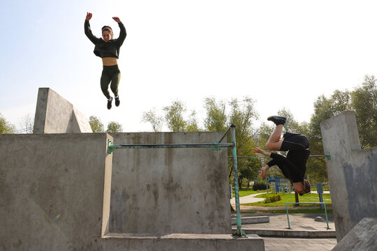 A guy and a girl jump on a sports field on the street