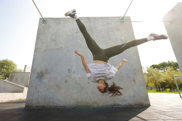A girl jumps upside down against a concrete wall