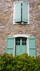 Fototapeta na wymiar Old house with windows and green shutters. Traditional exterior of rural house, France. Facade of medieval stone building with flowers. Retro residential design. French traditional architecture. 
