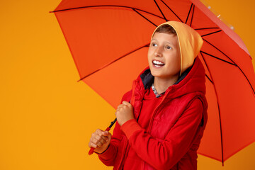happy emotional cheerful boy in autumn clothes laughing under a red umbrella