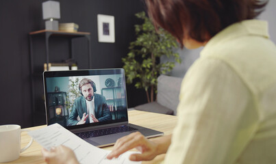 Overshoulder view of woman holding papers talking to male business partner using video call