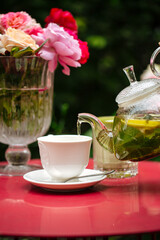 Pouring green tea in white cup on table with roses