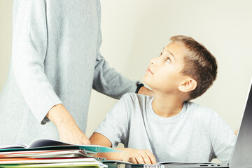 Kid learning online with laptop computer at home. Mother help him, explains task. Technology, remote education, distance learning, home studying