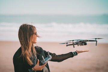 Young modern lady pilot in black jacket lands drone on her hand with remote controller near the...