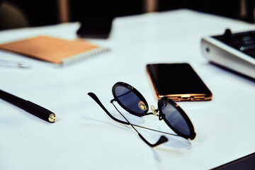 Close up of stylish sunglasses, pen and smartphone on a table in radio station studio