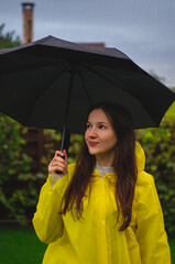 a young woman in a rainy weather in a yellow raincoat holding an umbrella