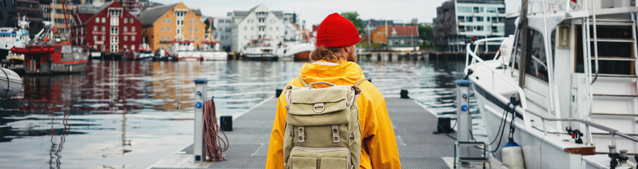 Man tourist with touristic rucksack wearing yellow jacket walking among authentic fishing boats. Wide image