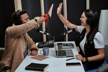 Portait of two cheerful radio hosts, young man and woman giving high five while talking, moderating...