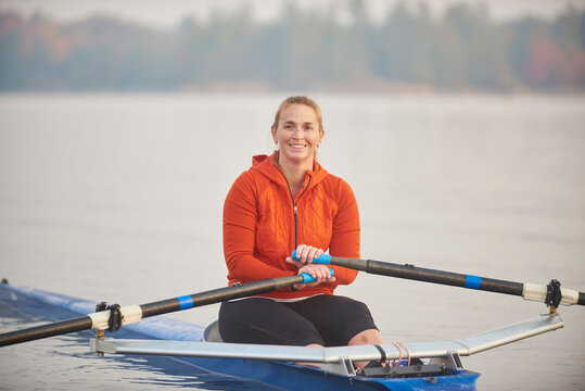 Portrait of a smiling middle aged woman sitting in a single scull on lake at sunrise.