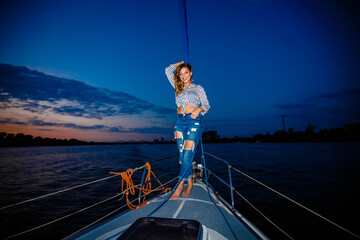 a girl in jeans stands on a yacht and looks at the evening sunset