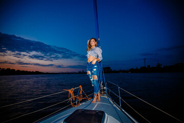 a girl in jeans stands on a yacht and looks at the evening sunset
