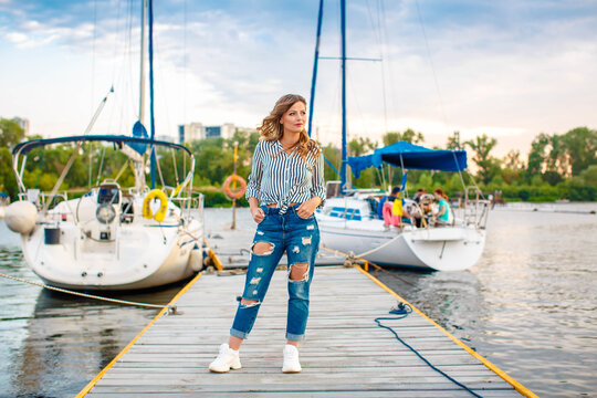 a girl in a shirt and jeans stands on the pier near the yachts