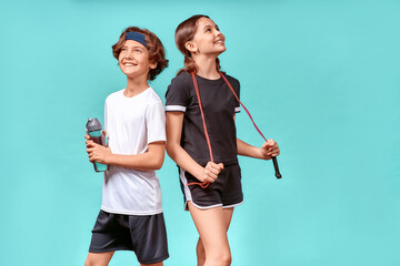 Resting after workout. Two teenagers, boy and girl with jumping rope and bottles of water looking away and smiling while posing isolated over blue background - Powered by Adobe