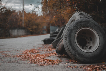 Discarded old tires lie on top of each other as if in a landfill, in the foreground is a large dirty used truck wheel