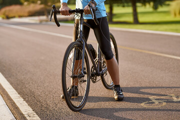 Cycling outdoors. Cropped shot of a man in sportswear standing with his road mountain bike on the road in park