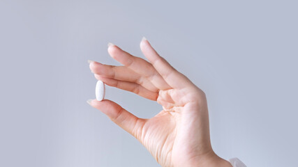 Woman in white blouse holding in hand magnesium or calcium supplement capsule. Bioactive additive...