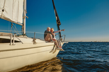 Sailing. Happy retired family couple sitting on the side of a sail boat or yacht deck floating in a...